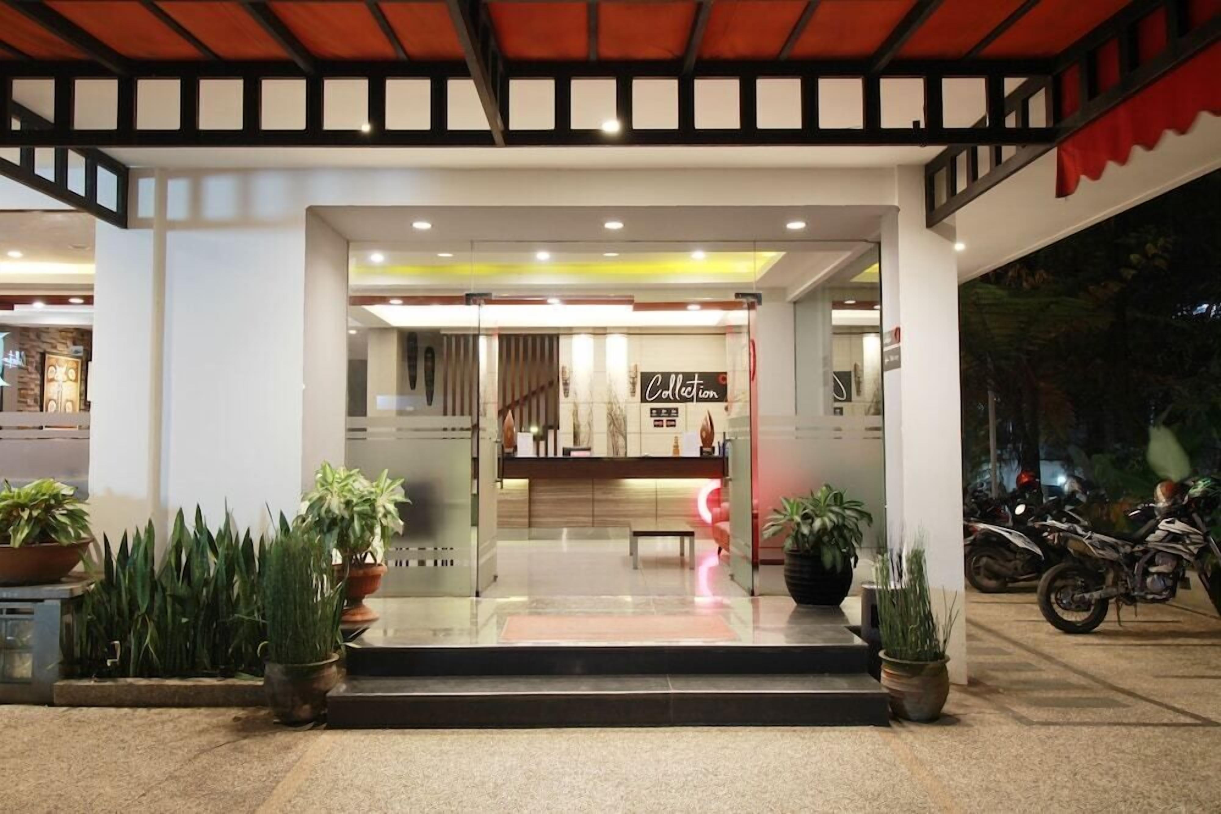 A hotel entrance with a reception desk, potted plants, and a motorcycle parked outside.