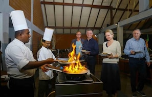 A group of people in a kitchen with a large flame on a pan. - Elephas Resort & Spa (Avudangawa)
