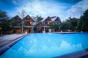 A large swimming pool with a wooden deck and a building with multiple balconies. - Elephas Resort & Spa (Avudangawa)