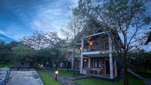 Uma casa de dois andares com varanda, cercada por árvores e um gramado bem cuidado.