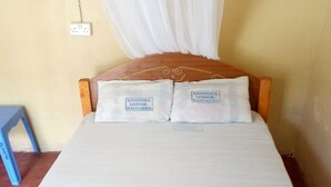 A bed with two pillows labeled "Heshima Lodge Naivasha" and a blue stool to the left. - Heshima Lodge (Naivasha)