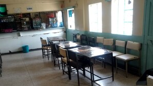 A dining area with a long table and chairs, a counter with various items, and windows with blinds. - Heshima Lodge (Naivasha)