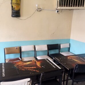 A room with four tables and chairs, a wall-mounted air conditioning unit, and a Guinness beer bottle. - Heshima Lodge (Naivasha)
