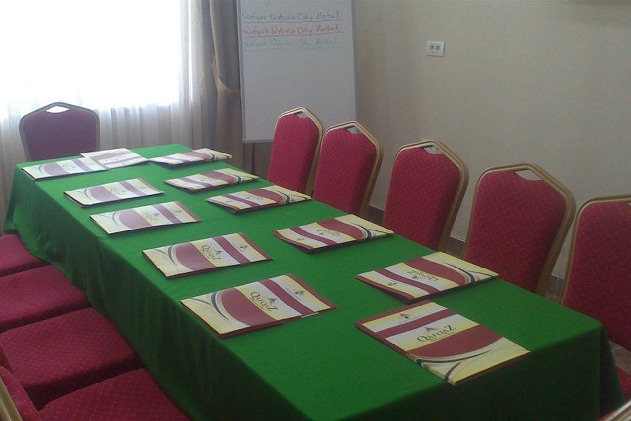 A conference room with a long table covered with green tablecloths, red chairs, and nameplates.
