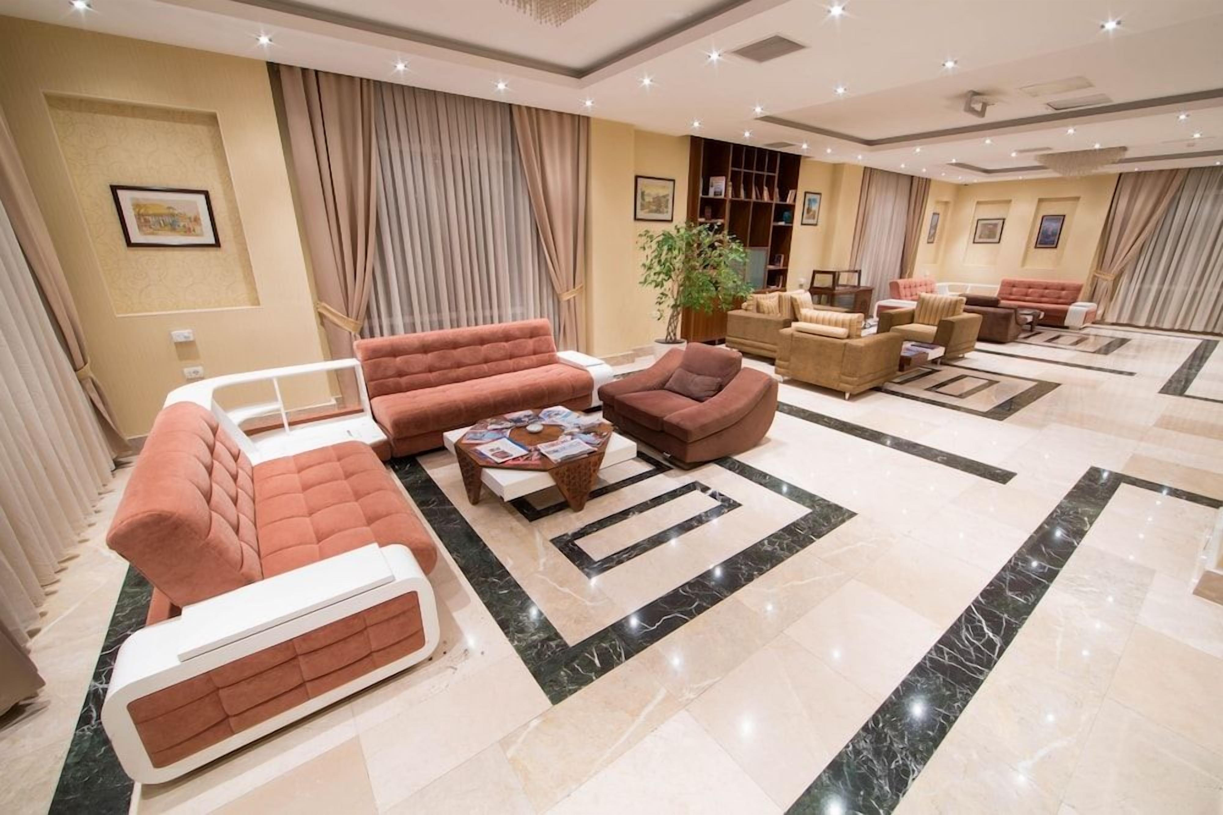 A spacious hotel lobby with multiple seating areas, a central coffee table, and a large plant.