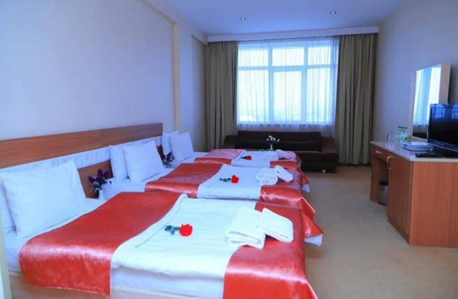 A hotel room with three beds, a TV, and a large window with curtains.