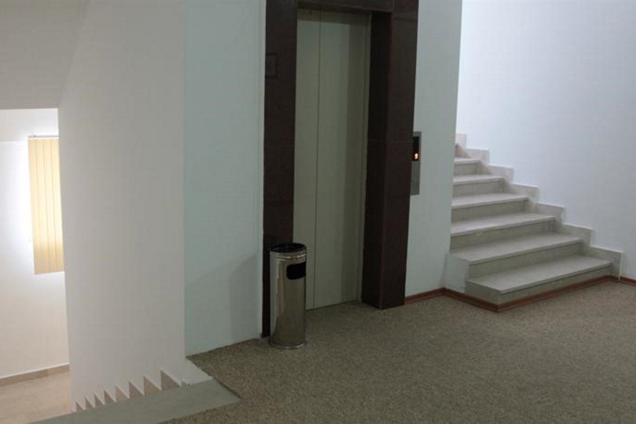 A staircase leading to an elevator in a room with a carpeted floor and a trash can.