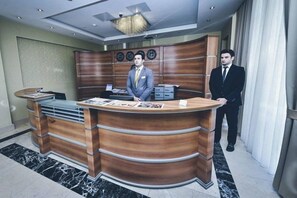 Un mostrador de recepción con detalles de madera, un reloj digital y una lámpara de araña moderna.