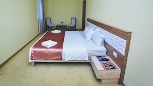A hotel room with a large bed, two chairs, a small table, and a nightstand with a magazine. - Gabala City Hotel (Gabala)