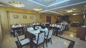 Un comedor con varias mesas y sillas, una araña de techo y un papel tapiz decorado.