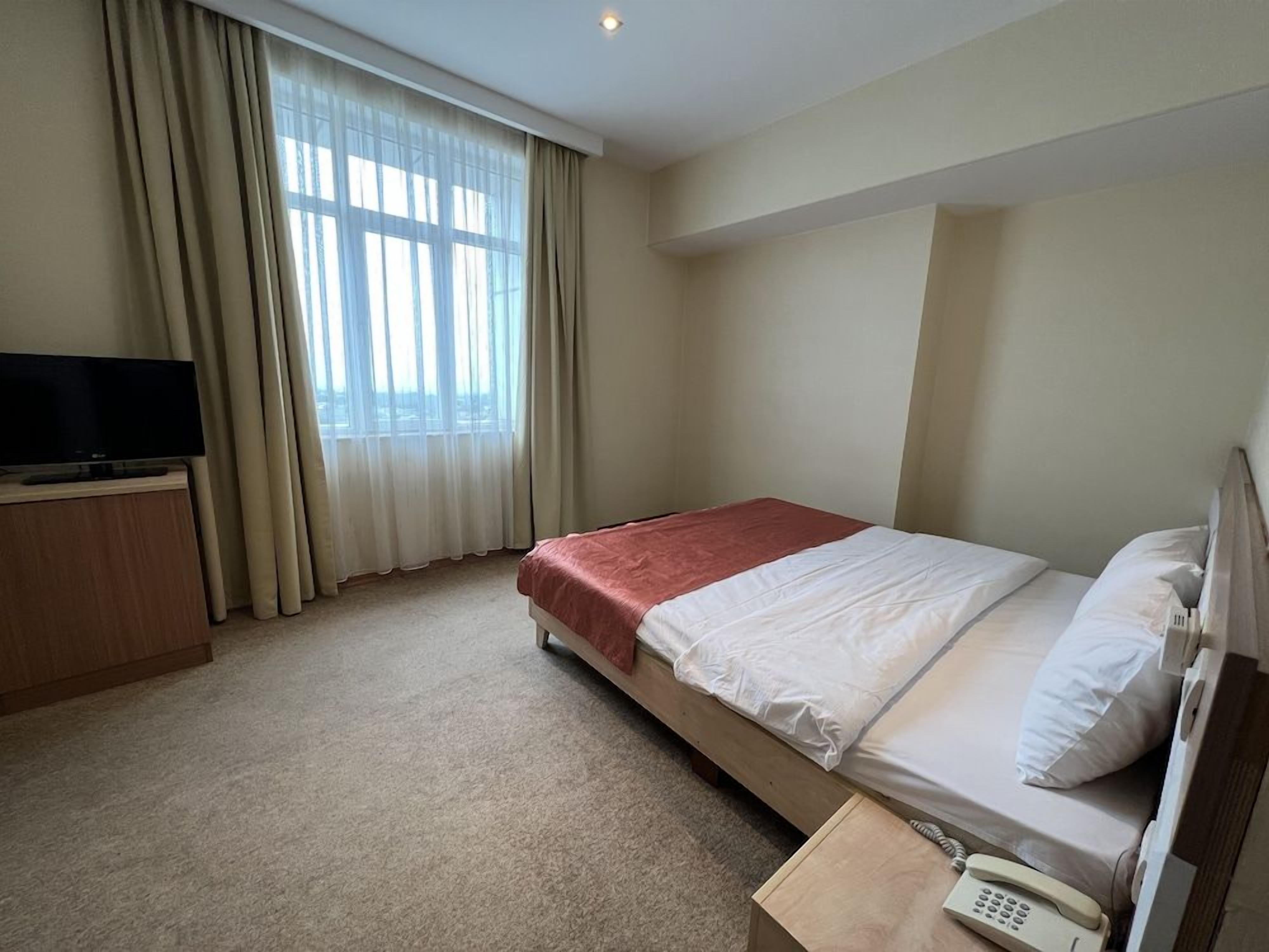A hotel room with a bed, a television, a telephone, and a window with curtains.