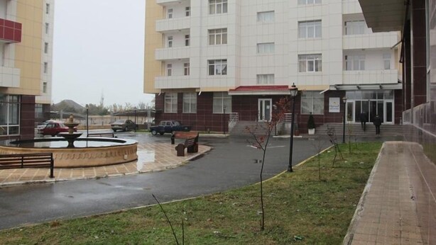 Un edificio residencial de varios pisos con un patio central, una fuente y una zona de estacionamiento.