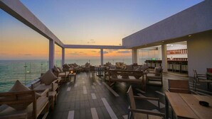 En terrasse med siddepladser og borde med udsigt over havet, præget af moderne arkitektur med store glasvinduer.