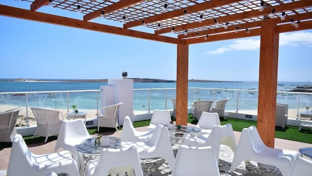 A covered outdoor seating area with white chairs and tables, overlooking the sea. - Ouril Hotel Agueda (Boa Vista)