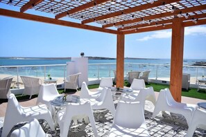A covered outdoor seating area with white chairs and tables, overlooking the sea. - Ouril Hotel Agueda (Boa Vista)