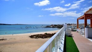 A beach view with a clear sky, a sandy shore, and a wooden pergola with white chairs. - Ouril Hotel Agueda (Boa Vista)