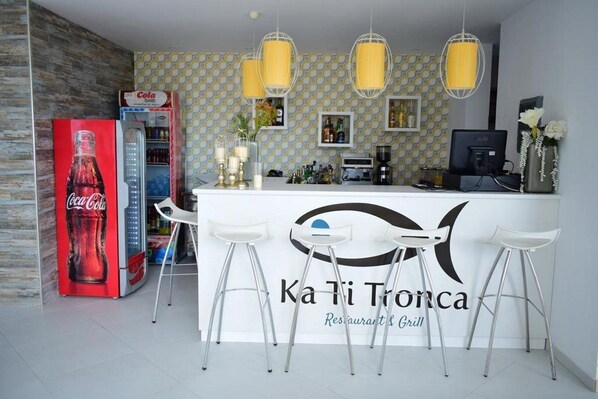 A restaurant bar area with a Coca-Cola vending machine, bar stools, and a counter with a logo. - Ouril Hotel Agueda (Boa Vista)