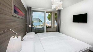Una habitación de hotel moderna con cama, televisor, ventana con vista al mar y balcón.