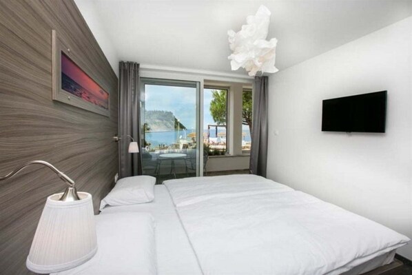A modern hotel room with a bed, a TV, a window with a view of the sea, and a balcony. - Barbara Piran Beach Hotel AND SPA (Piran)
