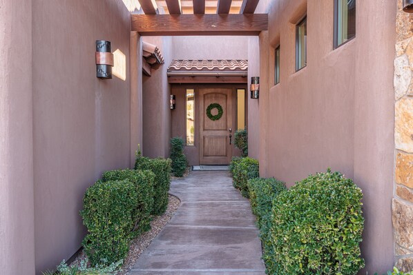 A narrow pathway leading to a wooden door with a wreath, flanked by stone walls and green hedges. - Stunning 5BR+Loft, Sleeps 16 w/ Casita on Hole 1 (St. George)