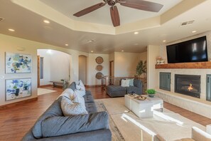 A spacious living room with a gray sectional sofa, a fireplace, a flat-screen TV, and artwork on the walls. - Stunning 5BR+Loft, Sleeps 16 w/ Casita on Hole 1 (St. George)