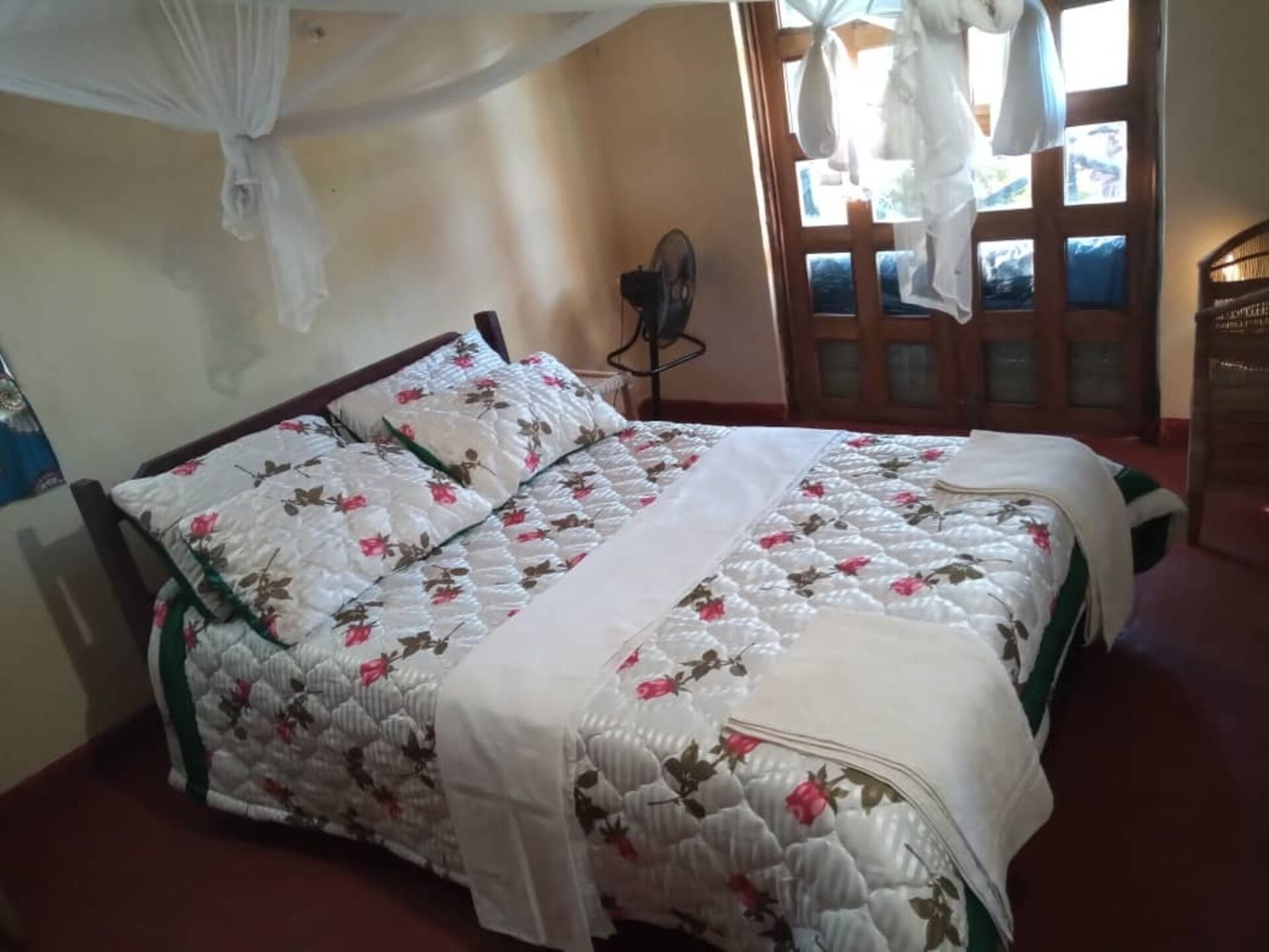 A bedroom with a bed covered in floral bedding, a wooden headboard, and a window with curtains.