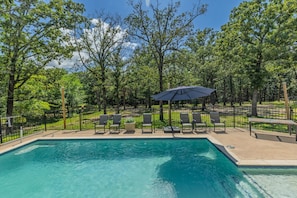 A swimming pool with lounge chairs and an umbrella, surrounded by trees.