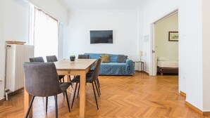 Ein Zimmer mit Esstisch aus Holz, Stühlen, einer blauen Couch und einem Bett.