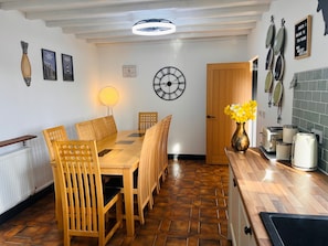 A dining area with a wooden table and chairs, a wall clock, and a vase of flowers. - Ty'n Rardd Mountain Views Secure Garden Parking (Beaumaris)
