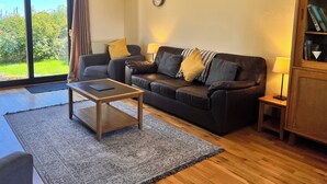 A living room with a sofa, coffee table, and lamps. There is a view through a glass door to the outdoors. - Ty'n Rardd Mountain Views Secure Garden Parking (Beaumaris)