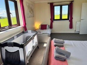 A room with a crib, a bed, a sofa, and a window with a view of a green field.