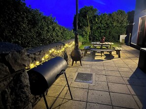 An outdoor patio with stone flooring, a grill, and string lights.