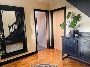 A hallway with a wooden floor, a black-framed mirror, a wooden door, and a potted plant on a cabinet.