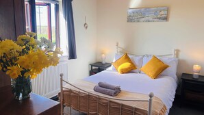 A bedroom with a bed, two bedside tables, a nightstand, a window with curtains, a vase of flowers, and a painting on the wall. - Ty'n Rardd Mountain Views Secure Garden Parking (Beaumaris)