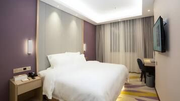 A modern hotel room with a large bed, bedside table, desk, chair, and a TV mounted on the wall.