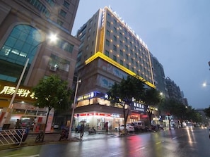 A multi-story hotel with a prominent yellow accent on the facade, a ground-level restaurant, and a wet street indicating recent rain. - Lavande Hotels Guangzhou North Railway Station (Guangzhou)