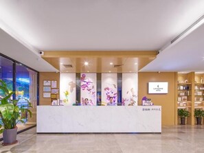 A reception desk with a white marble top, a sign above it, and potted plants on either side. - Lavande Hotels Guangzhou North Railway Station (Guangzhou)
