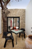 Un piccolo patio con un muro in pietra, una porta in vetro, un tavolo, due sedie e un vaso grande.