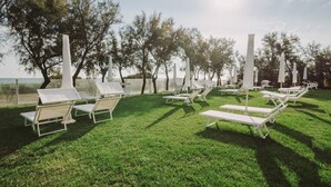 Een gazon met daaraan witte loungesteilen en hoge witte pilaren, waarschijnlijk onderdeel van een resort of hotel.