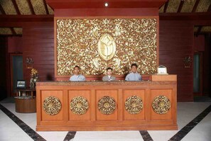 A reception desk with ornate golden carvings, a large emblem above, and a nameplate labeled "Welcome". - Pristine Lotus Spa Resort Inle (Nyaungshwe)