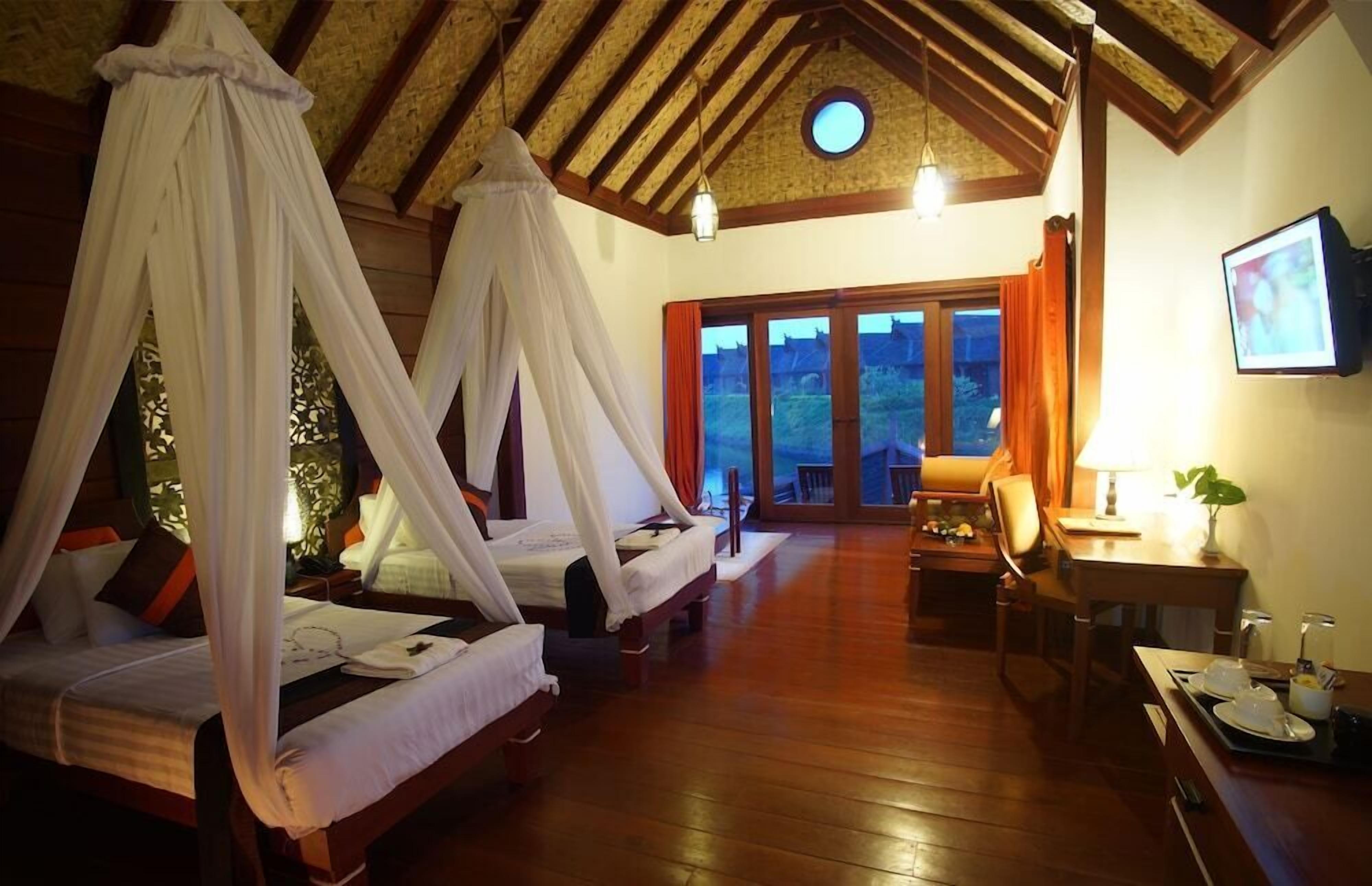 A room with two beds, a dining table, a TV, and a view of the outside.