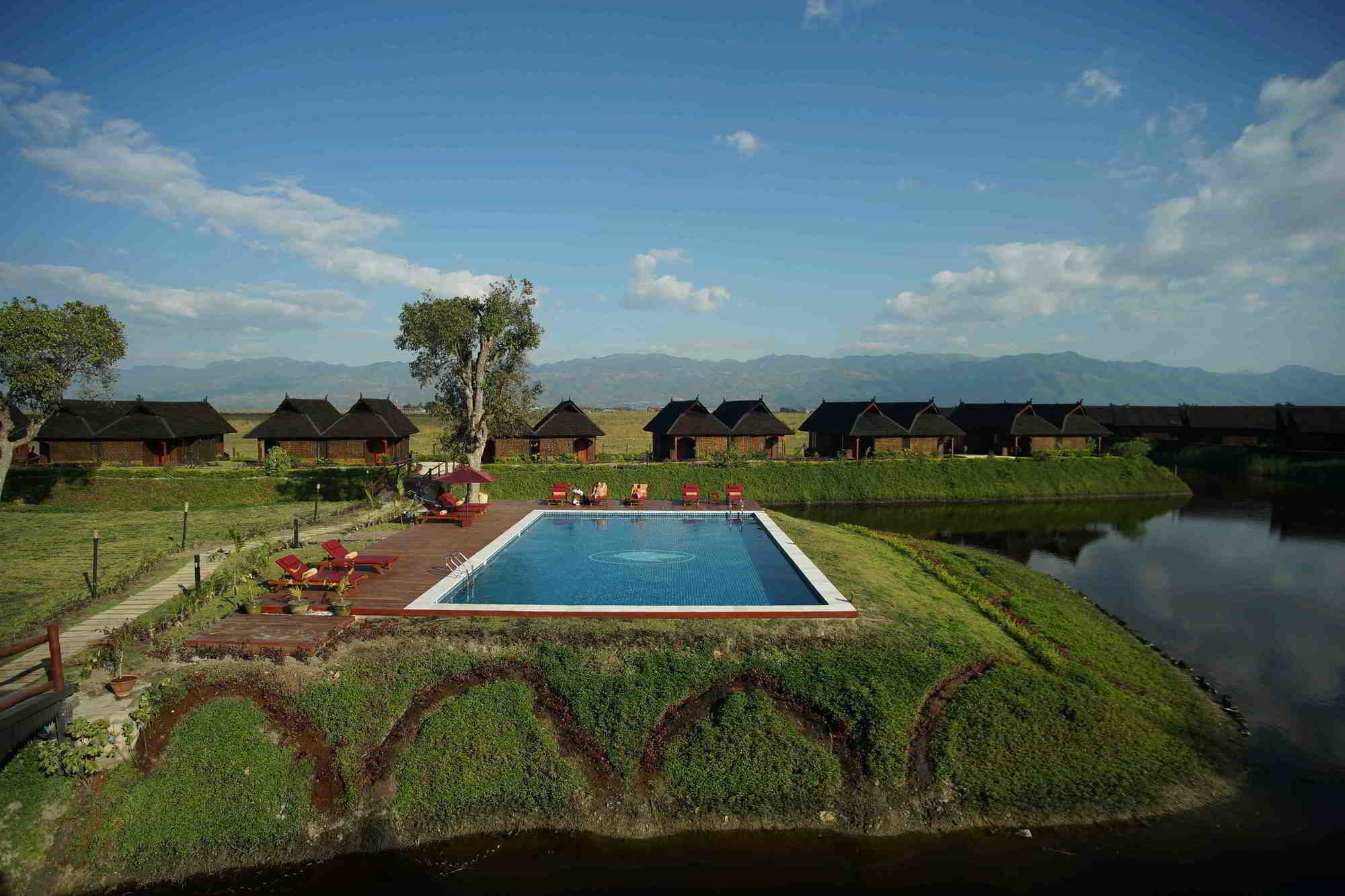 Une piscine entourée de chaises longues, une terrasse en bois et des petits chalets à toits de chaume, le tout situé dans un cadre rural.