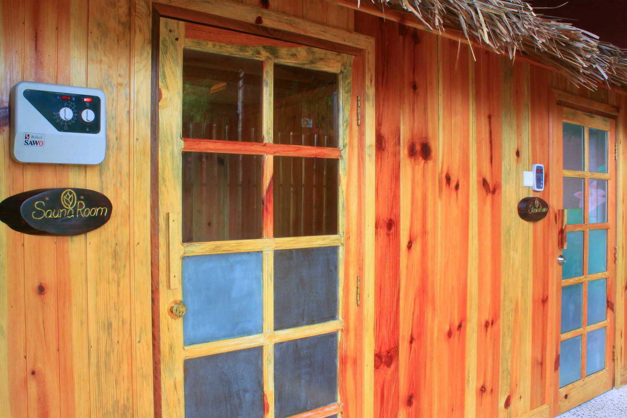 Un bâtiment en bois avec une grande porte vitrée, un panneau indiquant la présence d’un sauna et un panneau indiquant l’entrée d’une pièce.