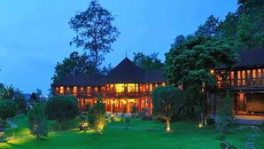 A large, multi-story building with a dark roof and illuminated windows, surrounded by well-maintained gardens and trees.