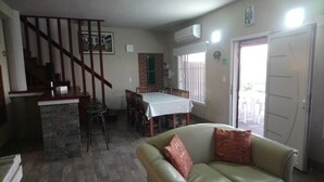 Ein Essbereich mit Tisch und Stühlen, einer Treppe, einer Couch und einer zur Außenseite führenden Tür.