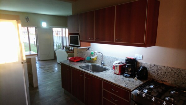 A kitchen with wooden cabinets, a granite countertop, a sink, a stove, and a television above the counter.