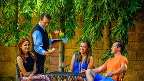 A group of people seated at an outdoor table with drinks, surrounded by greenery and a stone wall. - Gardenia Inn Hotel (San Salvador)