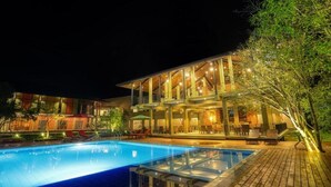 A multi-story hotel with a pool area, outdoor seating, and a well-lit facade. - Tropical Life Resort And Spa (Dambulla)