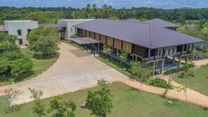 A modern building with a flat roof and a covered outdoor area, surrounded by greenery and palm trees. - Tropical Life Resort And Spa (Dambulla)