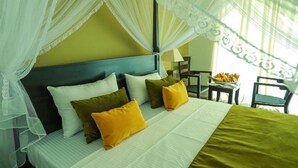 A bed with a canopy, pillows in various colors, and a bedside table with a lamp. - Tropical Life Resort And Spa (Dambulla)